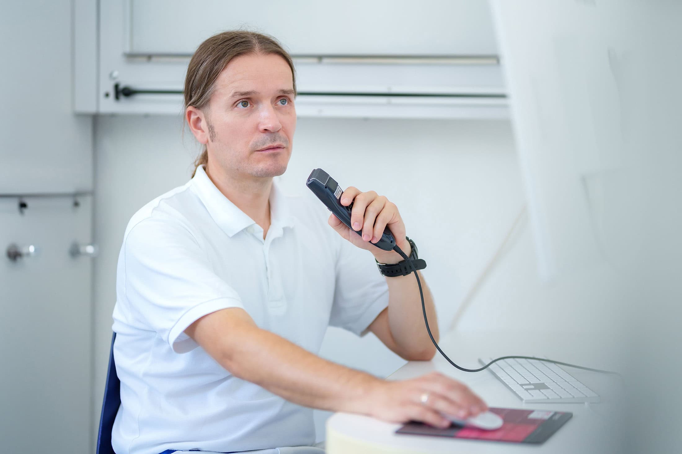 Arzt sitzt am Schreibtisch und spricht einen Befund über ein Diktiergerät